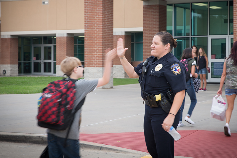 Female police officer high fiving a student on in the crosswalk in front of school